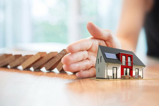 Schützende Hand vor einem Modellhaus.